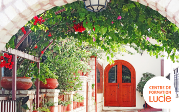 Porte rouge au fond de l'image et une arche remplie de verdure et fleurs en premier plan